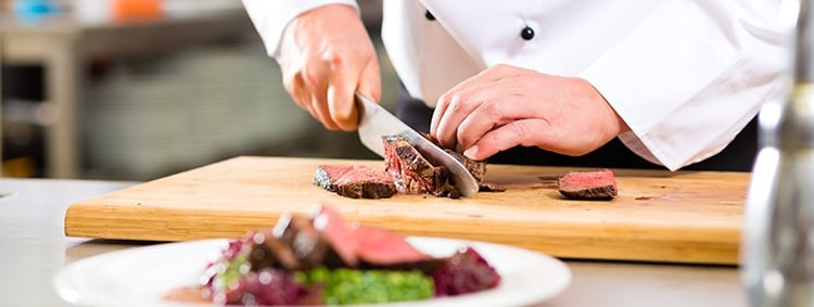 Chef cutting steak on cutting board with plate in view